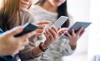 A group shot of three teenage girls looking down at mobile devices in their hands 